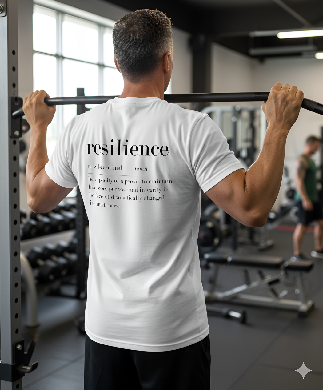 Man in a gym wearing a white t-shirt with 'resilience' text on the back.