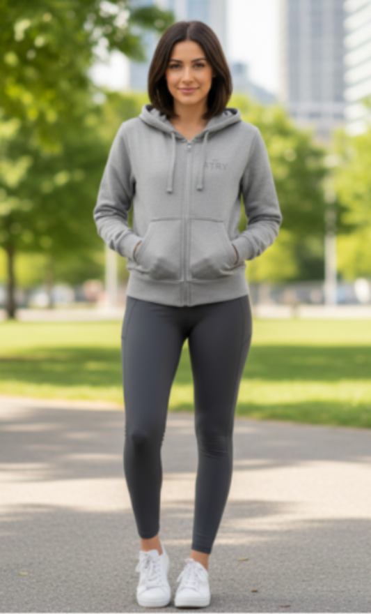 Woman wearing a gray hoodie and leggings standing outdoors with trees and buildings in the background